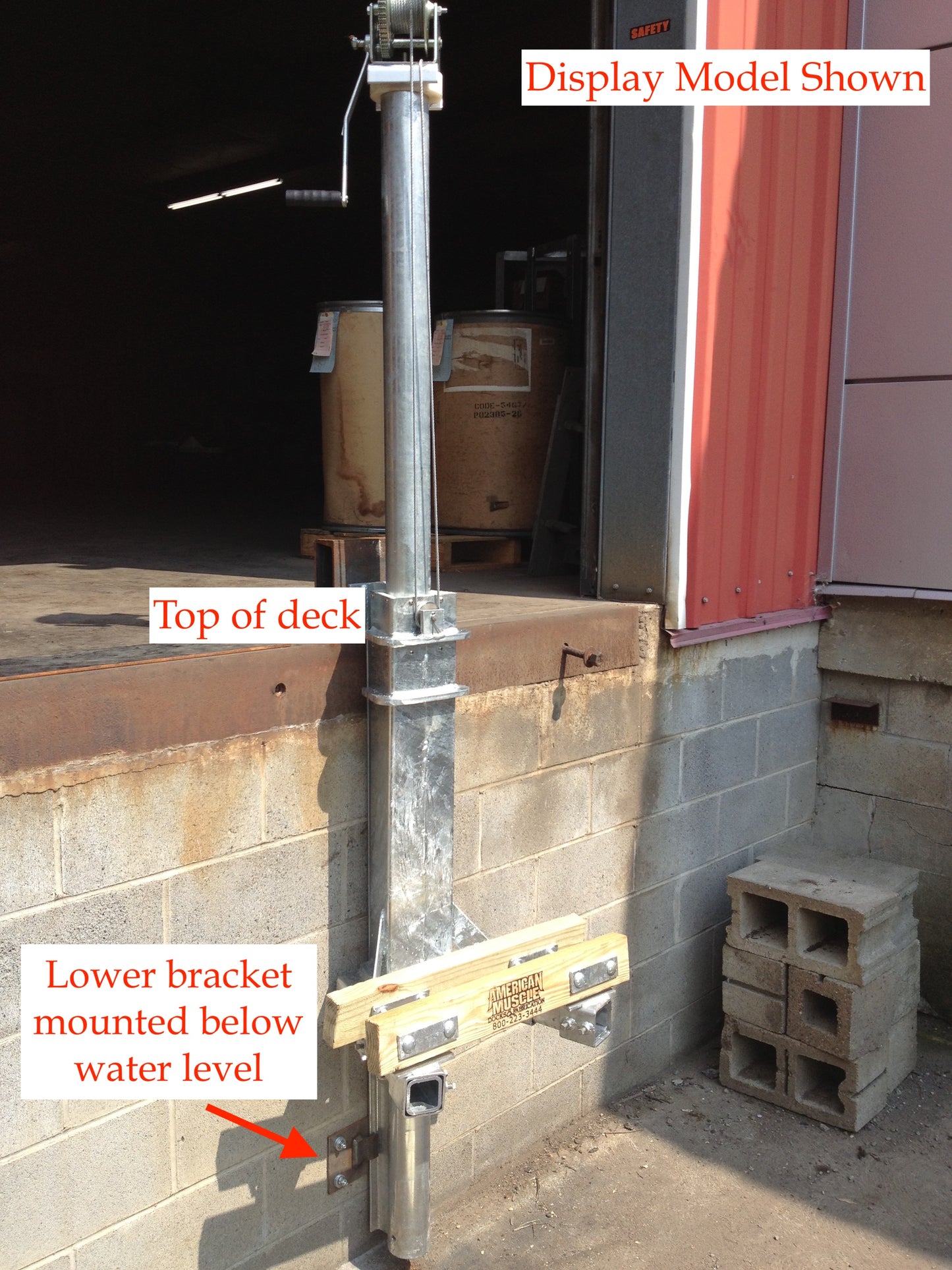 The Mr. Lifter - Manual 9' Pipe Track by American Muscle Docks & Fabrication is a rotating PWC lift mounted on the side of a concrete dock, with labeled parts like the top deck and a lower bracket set below water level.