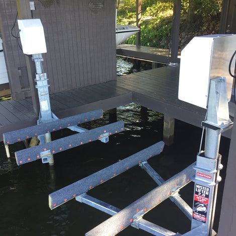Boat lift with metal beams and warning label extending over water beneath a wooden dock structure.