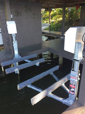 Boat lift with metal beams and warning label extending over water beneath a wooden dock structure.