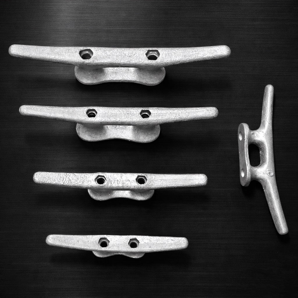 Four American Muscle Docks & Fabrication Cleat - Steel pieces are aligned horizontally, with a fifth set vertically on the right, against a dark background—showcasing marine-ready corrosion resistance.