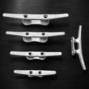 Four American Muscle Docks & Fabrication Cleat - Steel pieces are aligned horizontally, with a fifth set vertically on the right, against a dark background—showcasing marine-ready corrosion resistance.