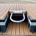 A metal mooring ring with a white roller is mounted on a floating dock made of brown composite planks and black plastic floats.