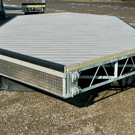 A metal and wood dock platform with a hexagonal shape is positioned on gravel outdoors, featuring metal support beams and a diamond plate side panel.