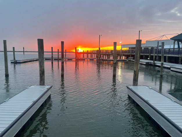 Empty boat docks and wooden piers over calm water at sunset, with an orange sun low on the horizon and a partly cloudy sky.