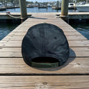 The New Era® Camo Flat Bill Snapback - Green from American Muscle Docks is displayed on a wooden dock with boats and water in the background.