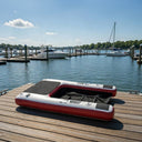 The Mutt-scle XL Floating Dog Ramp by American Muscle Docks & Fabrication is set up beside a marina, floating on calm water with boats nearby under a clear blue sky.