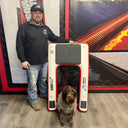 A man stands indoors next to the American Muscle Docks & Fabrication Mutt-scle XL Floating Dog Ramp, with a dog sitting in the cutout at the bottom center of this heavy-duty pool ramp.