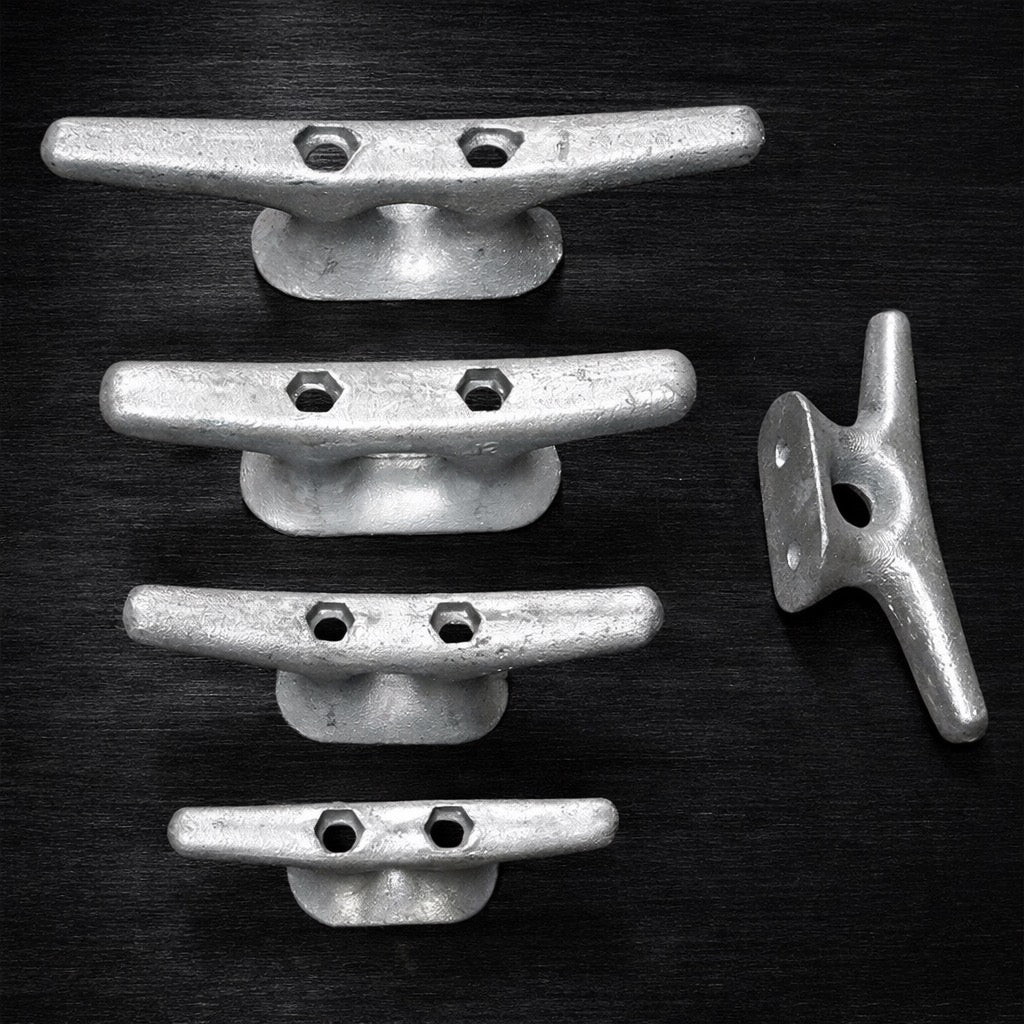 Four American Muscle Docks & Fabrication Cleat - Steel Ship dock cleats are vertically aligned on a dark surface, with a fifth cleat to the right, oriented differently.