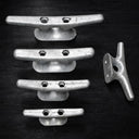 Four American Muscle Docks & Fabrication Cleat - Steel Ship dock cleats are vertically aligned on a dark surface, with a fifth cleat to the right, oriented differently.