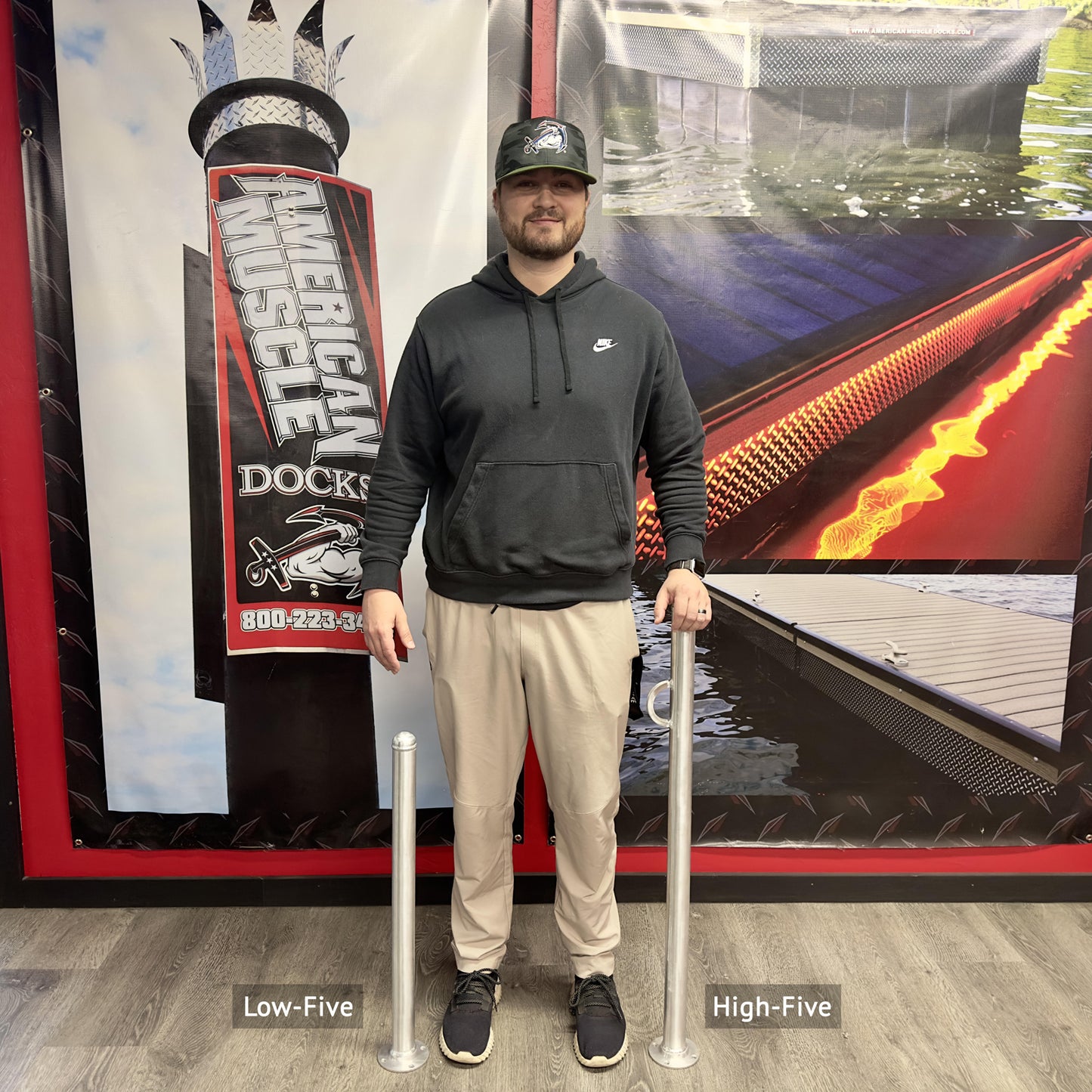 Man standing between two Helping Hand aluminum supoort assist poles with 'Low-Five' and 'High-Five' labels, in front of a promotional AMD backdrop.
