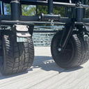 Close-up of two large black treaded caster wheels attached to the metal frame of an American Muscle Docks Collapsible Pull Wagon on a light-colored outdoor deck.