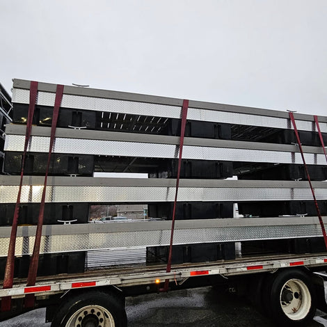 Several large metal structures are stacked and secured with red straps on a flatbed trailer, parked outdoors on a cloudy day.