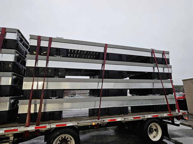 Several large metal structures are stacked and secured with red straps on a flatbed trailer, parked outdoors on a cloudy day.