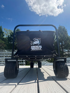 Collapsible Pull Wagon by American Muscle Docks with large wheels and a black bag, shown on a wooden deck under a partly cloudy sky.