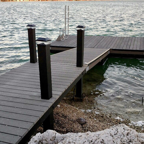 A wooden dock extends over a body of water with steps leading down and posts along the sides; small waves lap against the shore.