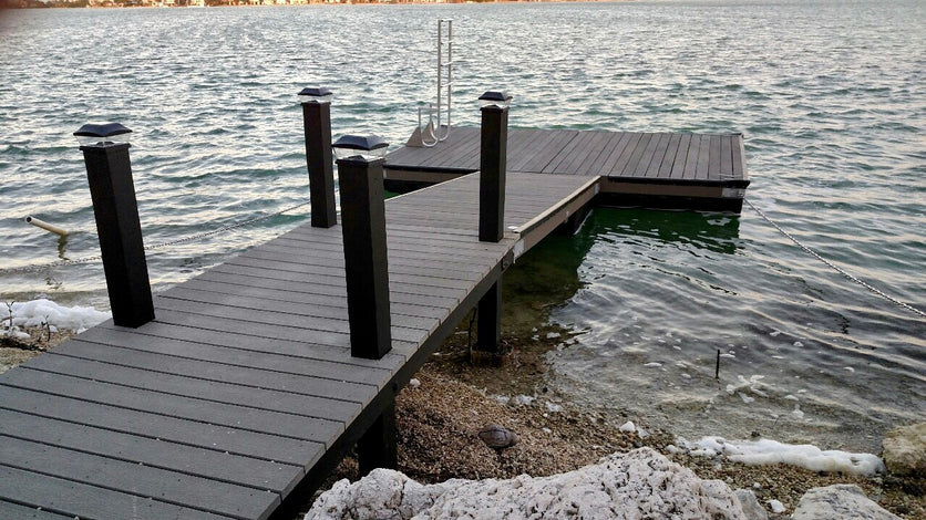 A wooden dock extends over a body of water with steps leading down and posts along the sides; small waves lap against the shore.